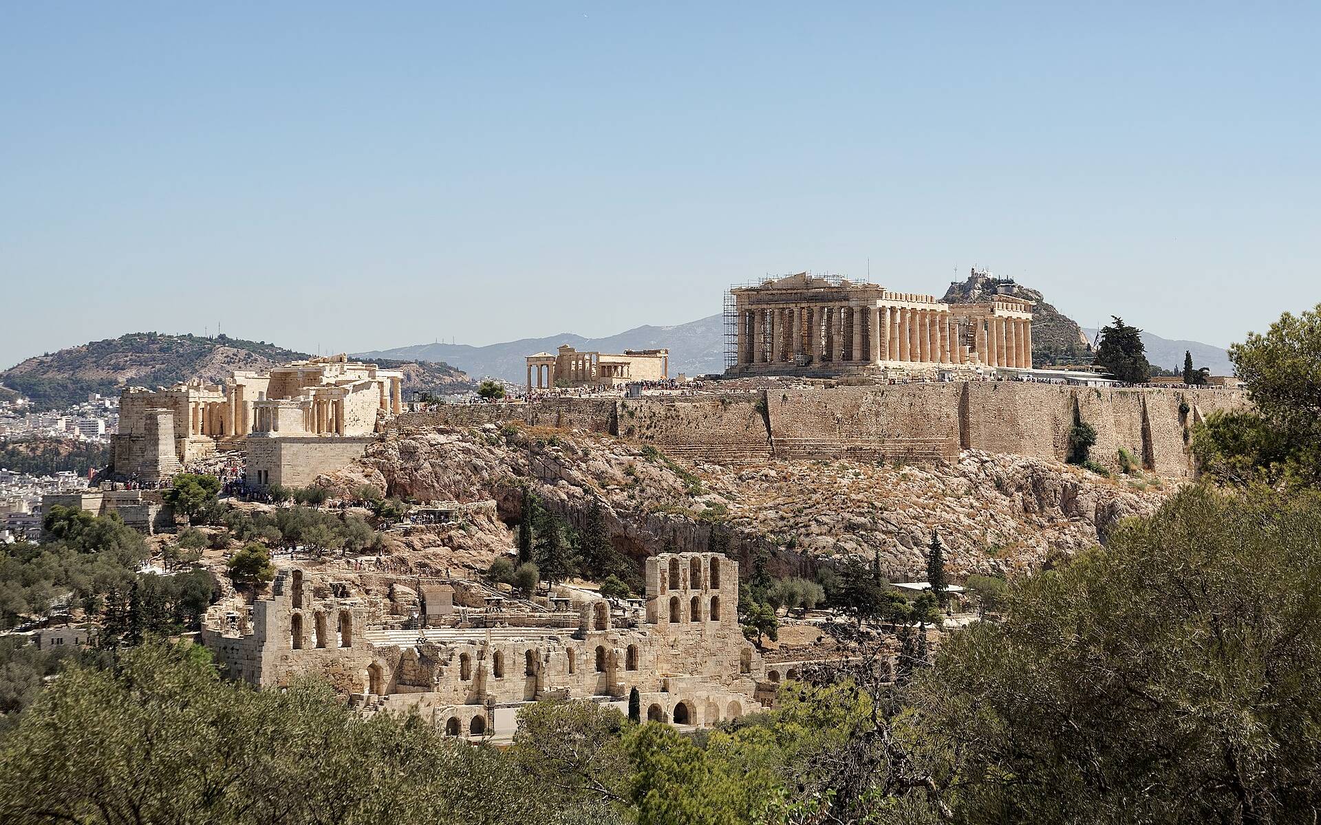 The Acropolis of Athens seen from Philopappos Hill under a clear sky, with the Parthenon and the Propylaea on the rock and the Odeon of Herodes Atticus below
