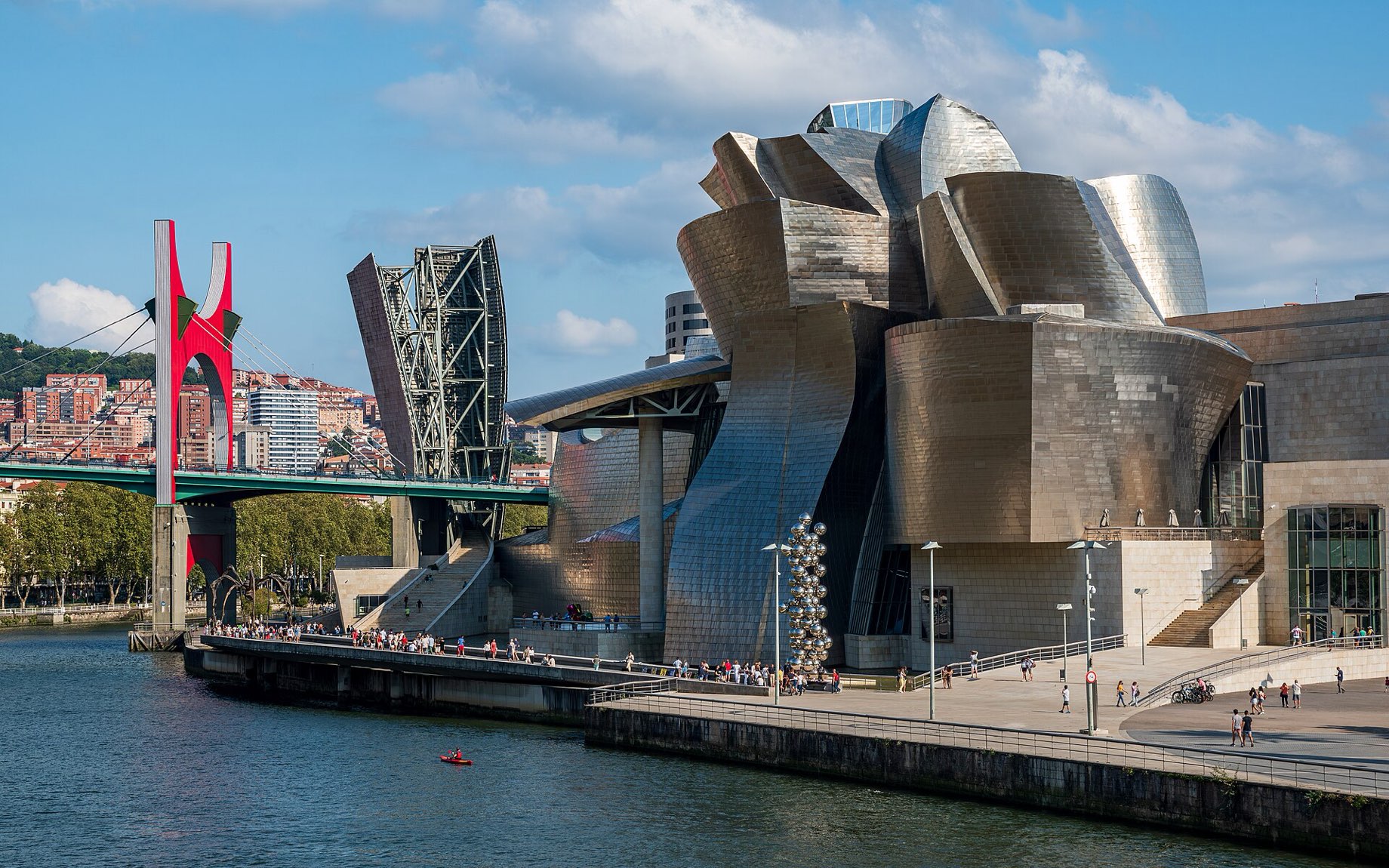 The titanium-clad Guggenheim Museum Bilbao on the bank of the Nervión, with the red arch of La Salve bridge to the left