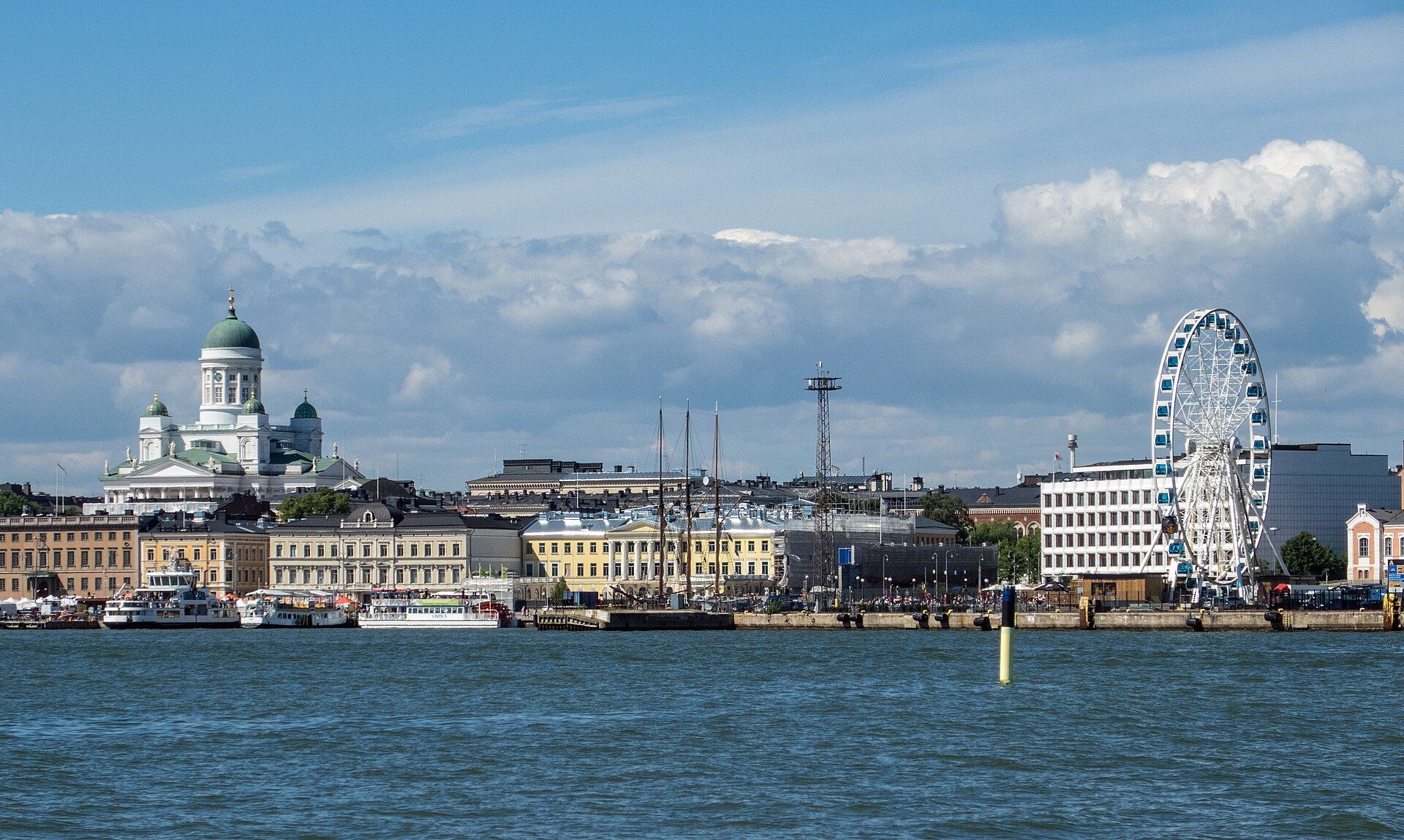 Helsinki seen from the sea: the white cathedral with its green domes above the Market Square waterfront, excursion boats at the quay and the SkyWheel on the right
