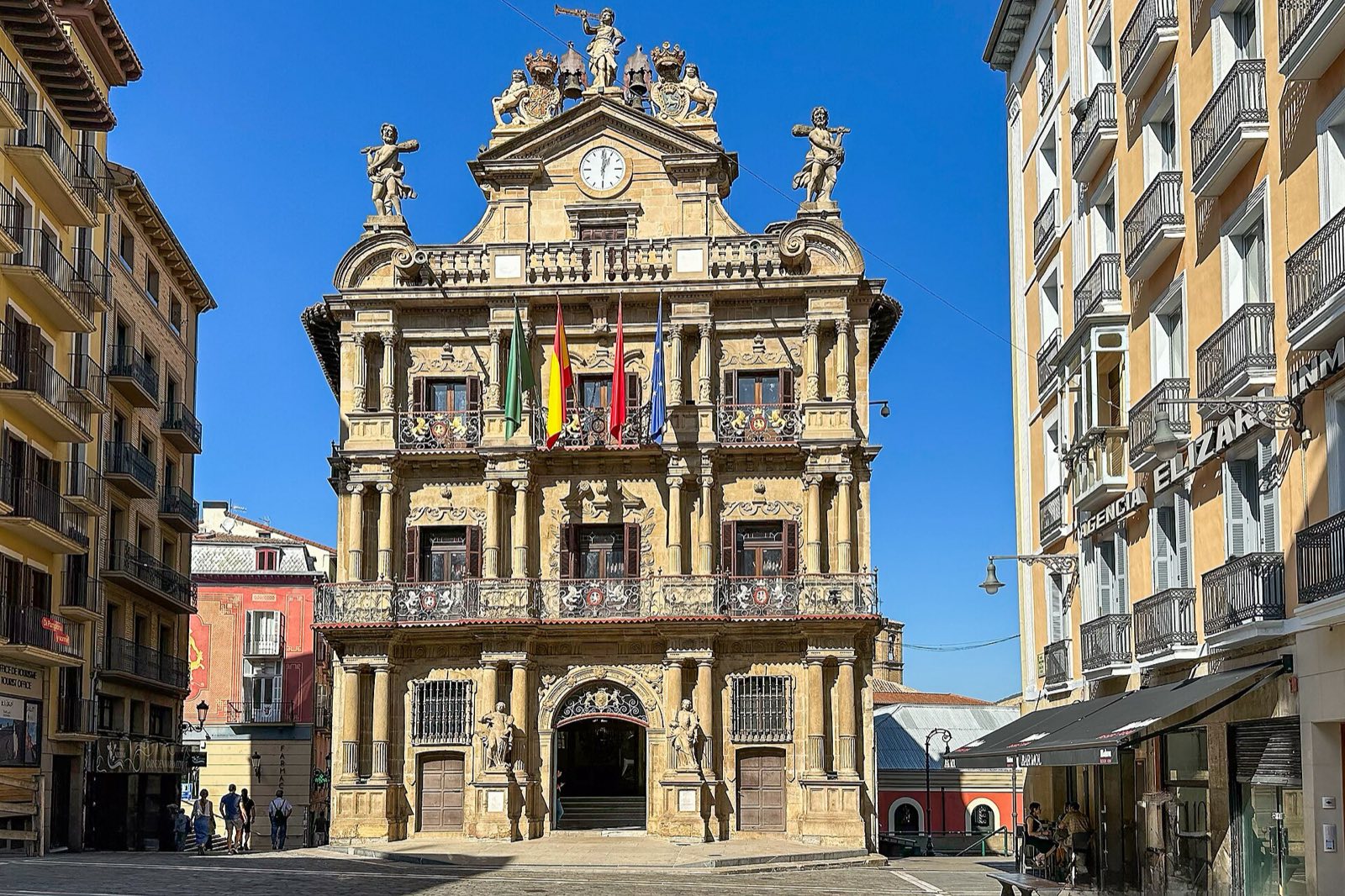 The baroque façade of Pamplona’s town hall, hung with flags, under a clear blue sky