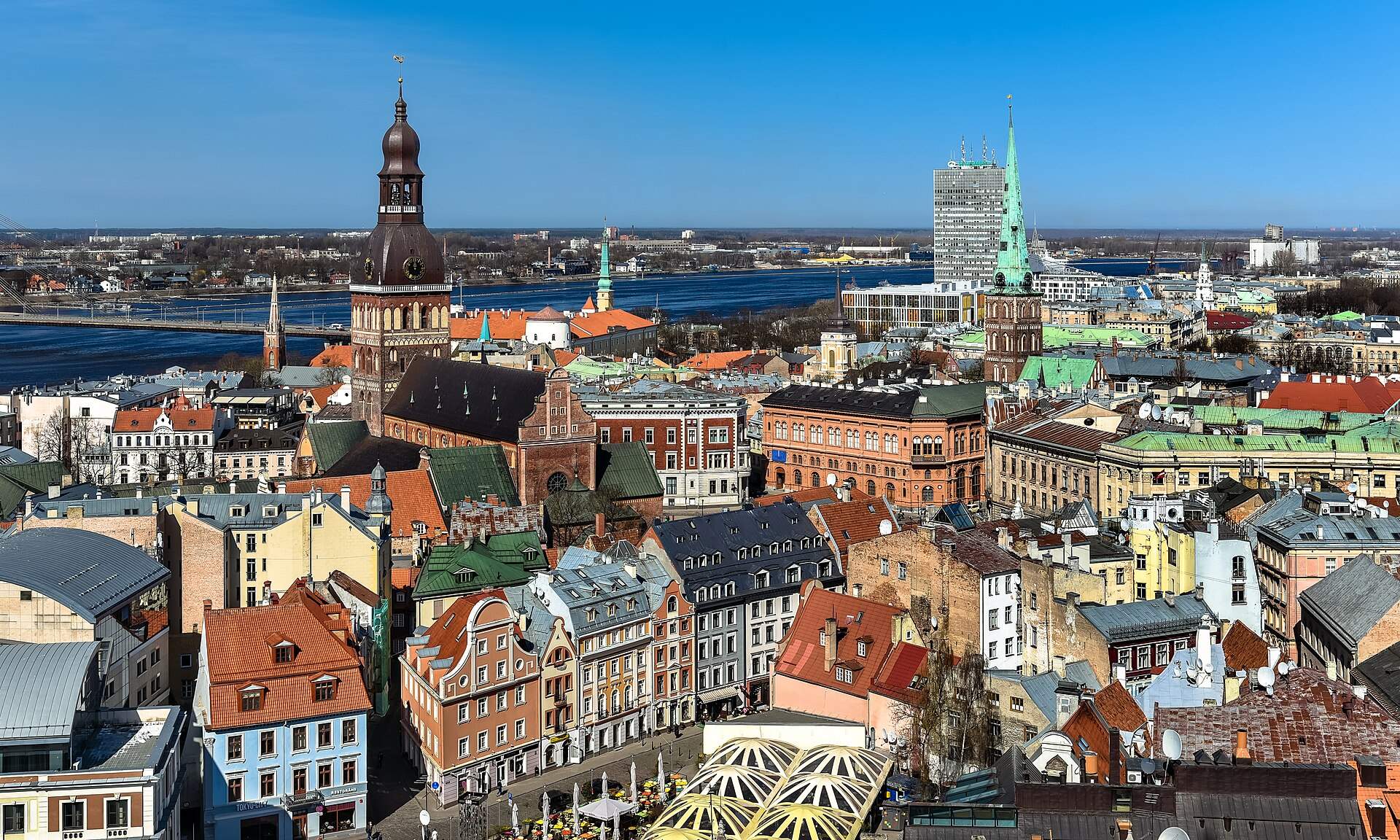 Rooftops of Riga’s Old Town in bright sunshine, with the tower of Riga Cathedral, the green spire of St James’s Cathedral and the Daugava river beyond