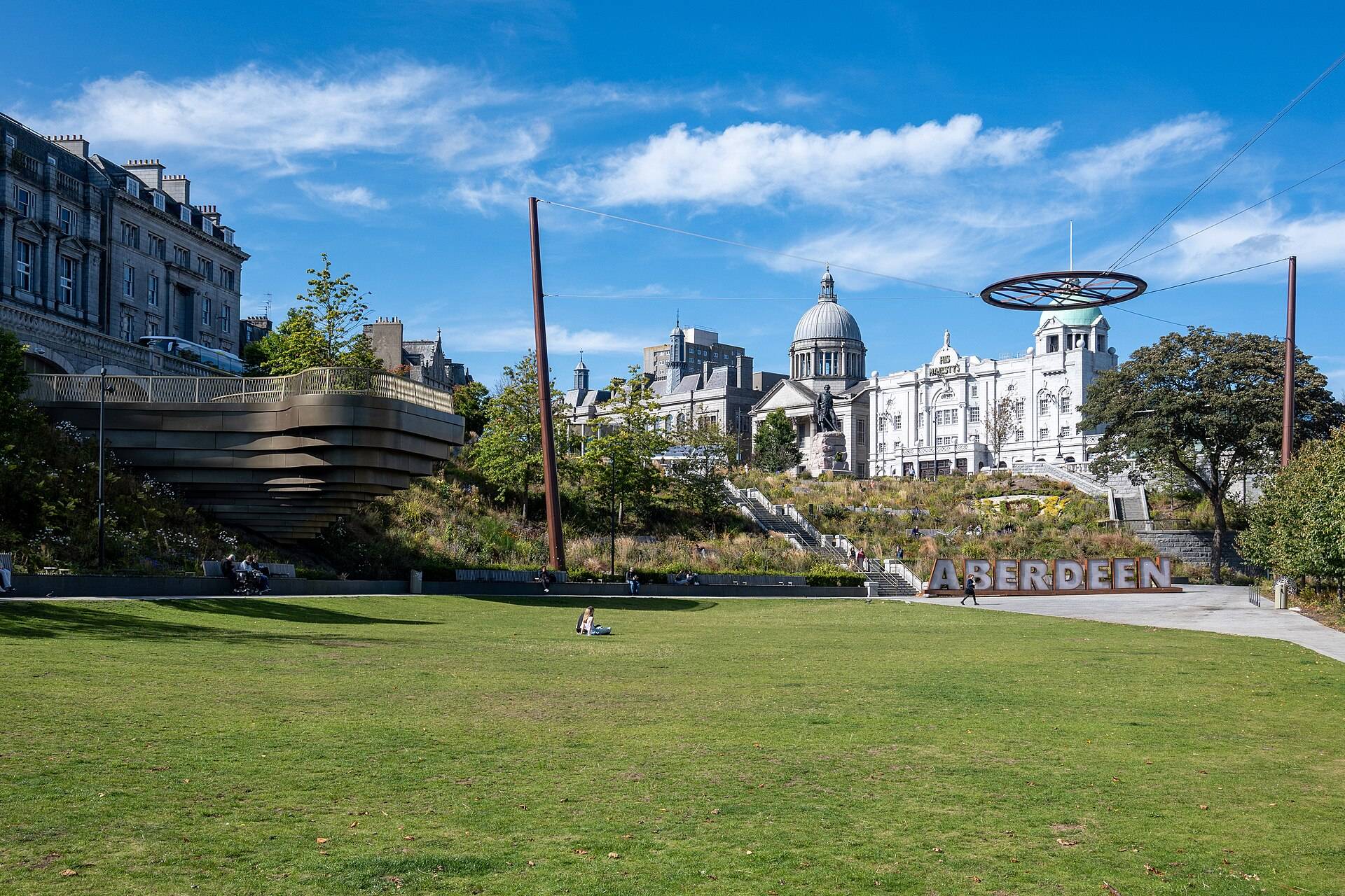 Union Terrace Gardens in Aberdeen on a sunny day, with the dome of St Mark’s Church and the pale granite front of His Majesty’s Theatre above the lawn and large letters spelling ABERDEEN