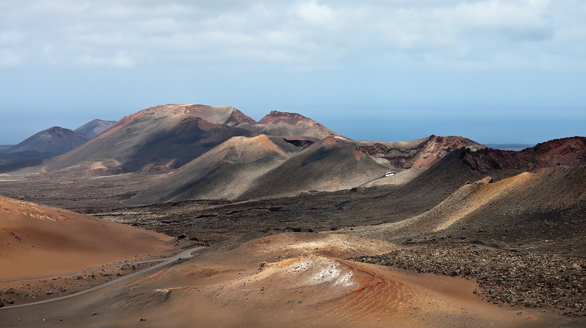 Volcanic cones in rust, ochre and grey in Timanfaya National Park on Lanzarote, with a road curving between them