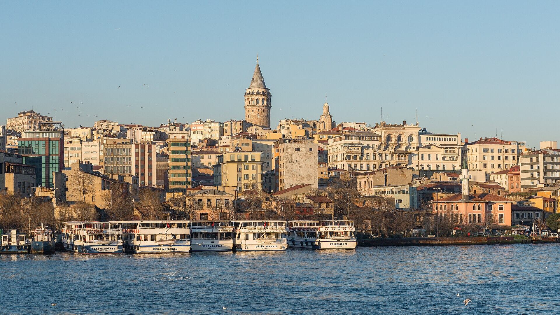 The Karaköy waterfront in Istanbul seen from the Golden Horn in late-afternoon light, with ferries moored at the quay and the Galata Tower above the rooftops